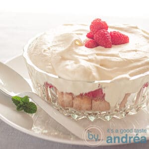square photo with a glass bowl with lady fingers, raspberries and whipped cream. Topped with fresh raspberries