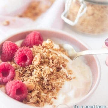A pink bowl with homemade granola filled with coconut and almond and topped with raspberries. In the right top extra granola