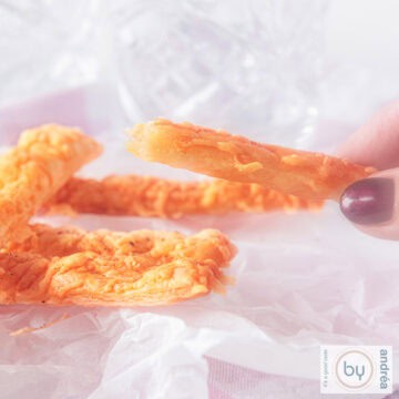 A square photo with a baking sheet with cheese sticks, half of which is being held.
