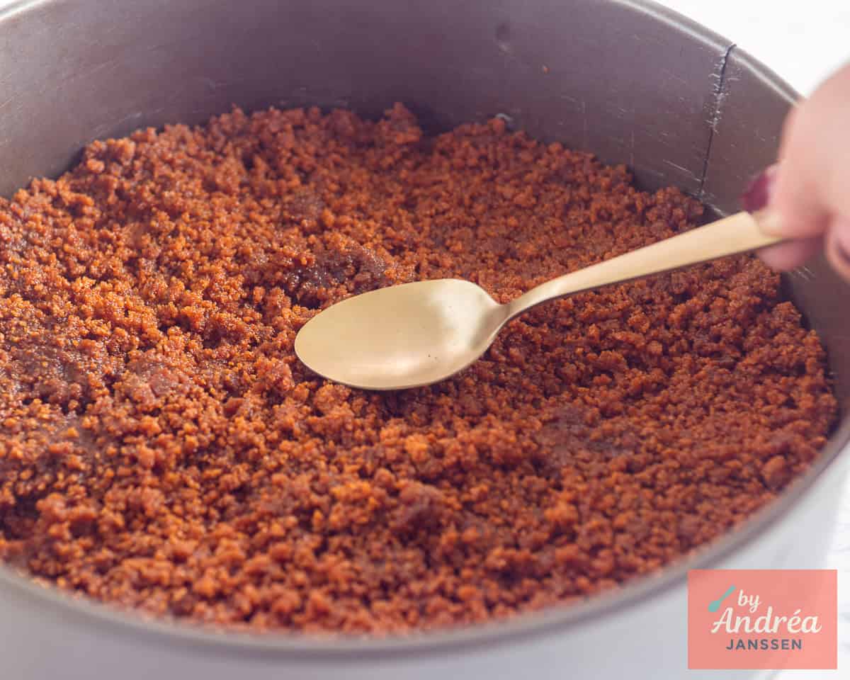 Bastognekoek bodem wordt aangedrukt in de springvorm met een lepel