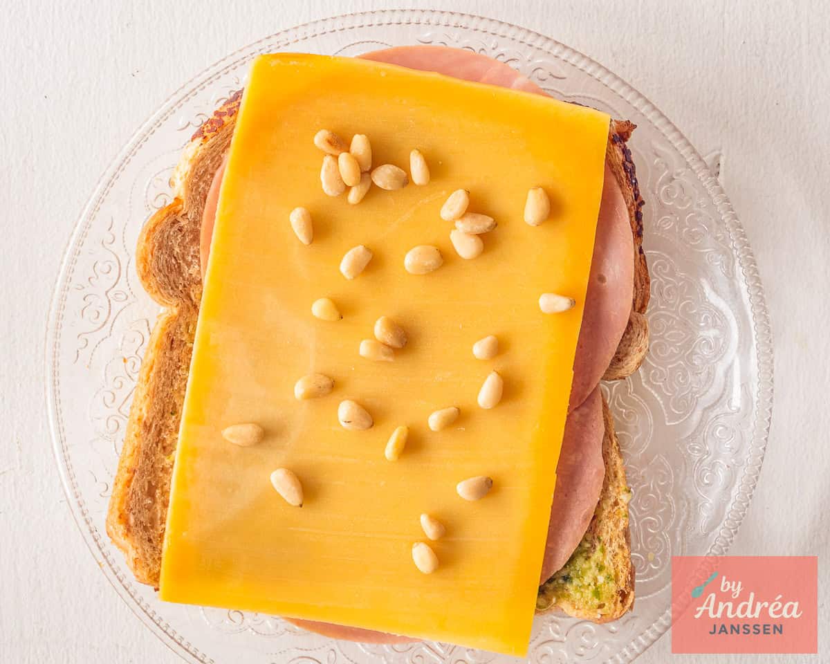 Layering the sandwich with pesto, ham, cheese and roasted pine nuts.