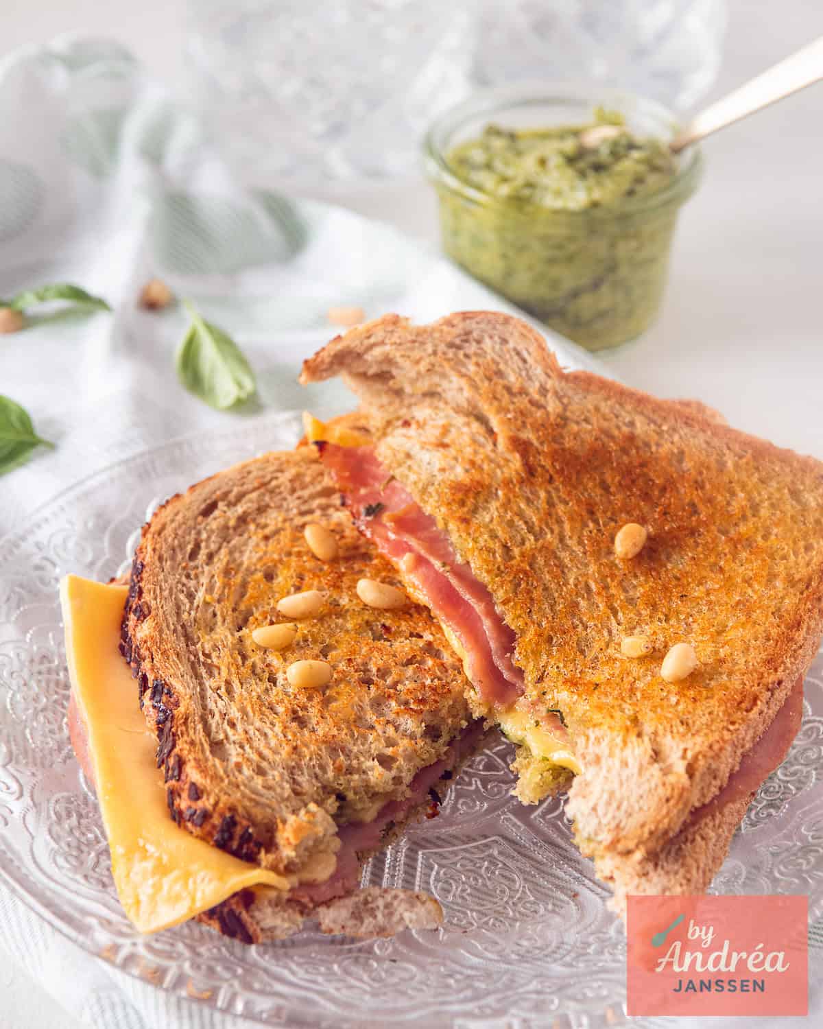 Two slices of a Ham Pesto Grilled Cheese Sandwich on top of each other on a glass plate