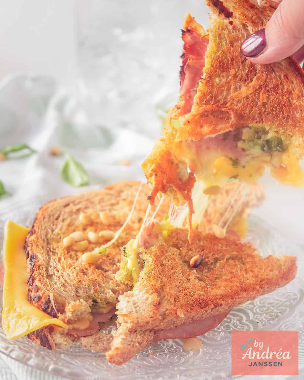 Two slices of grilled cheese with pesto and ham, one taken above cheesy strings appear.