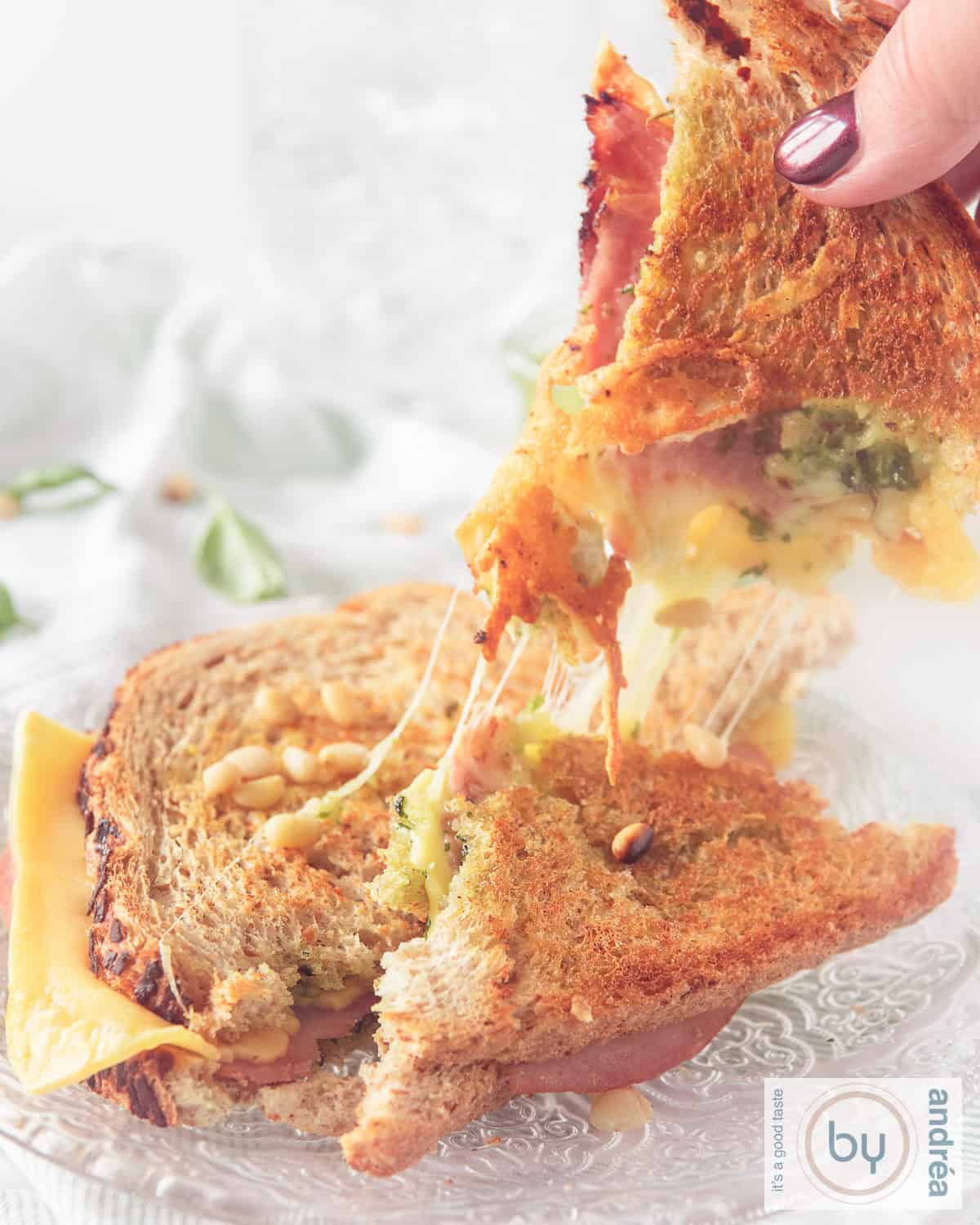 Eenfoto in de hoogte met een tosti met een afgebroken stuk die omhoog wordt gehouden. Slierten gesmolten kaas tussen de delen tosti