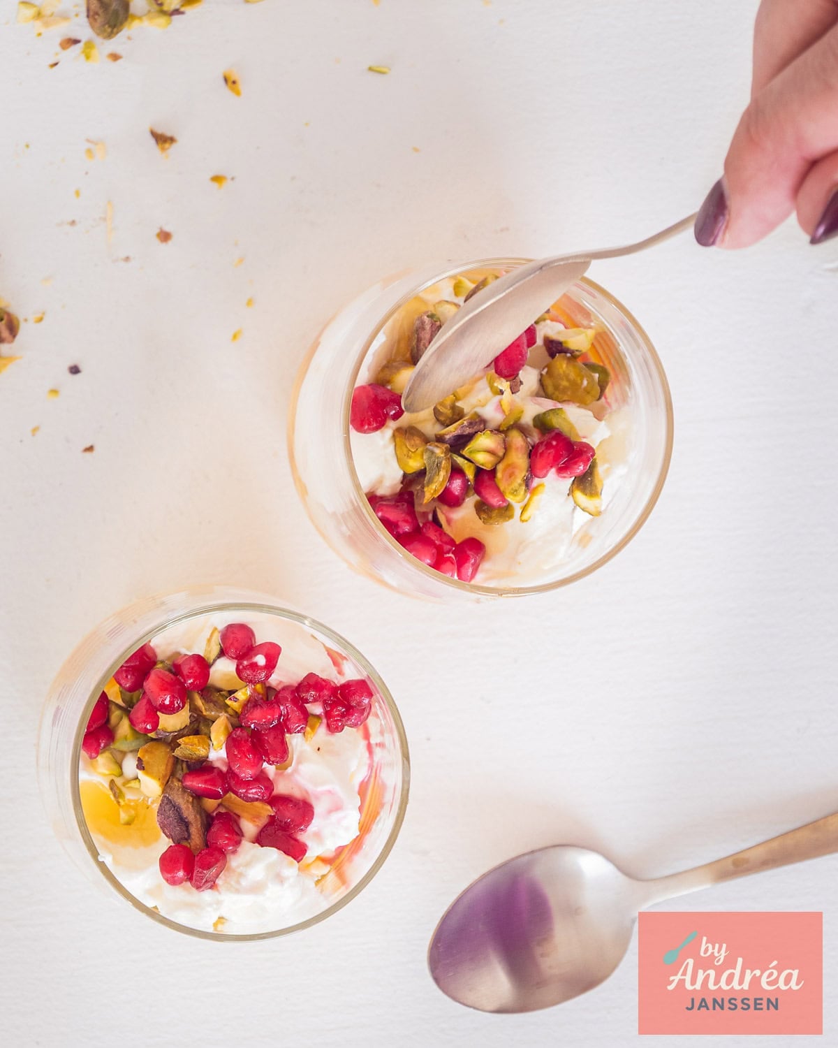 A photo from above with two dessert glasses filled with Dutch hangop, honey, pistachios, and pomegranate.