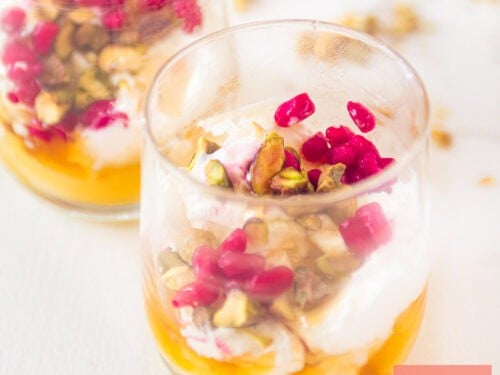 A square photo with two glasses positioned diagonally behind each other with Creamy strained yogurt with honey, pistachio, and pomegranate.