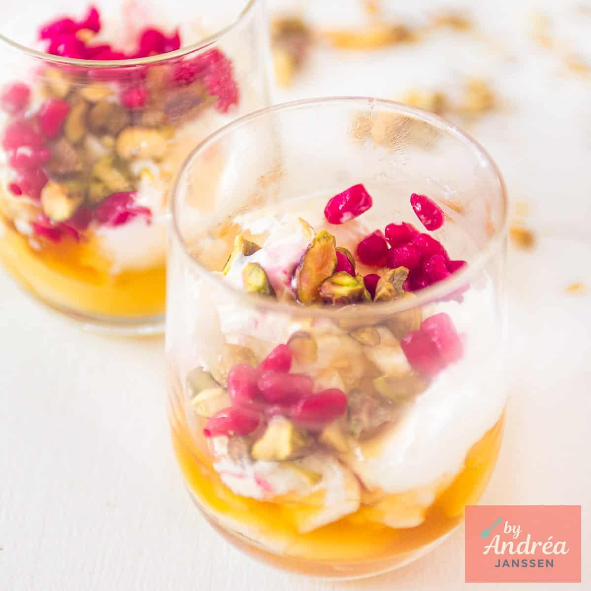 A square photo with two glasses positioned diagonally behind each other with Creamy strained yogurt with honey, pistachio, and pomegranate.