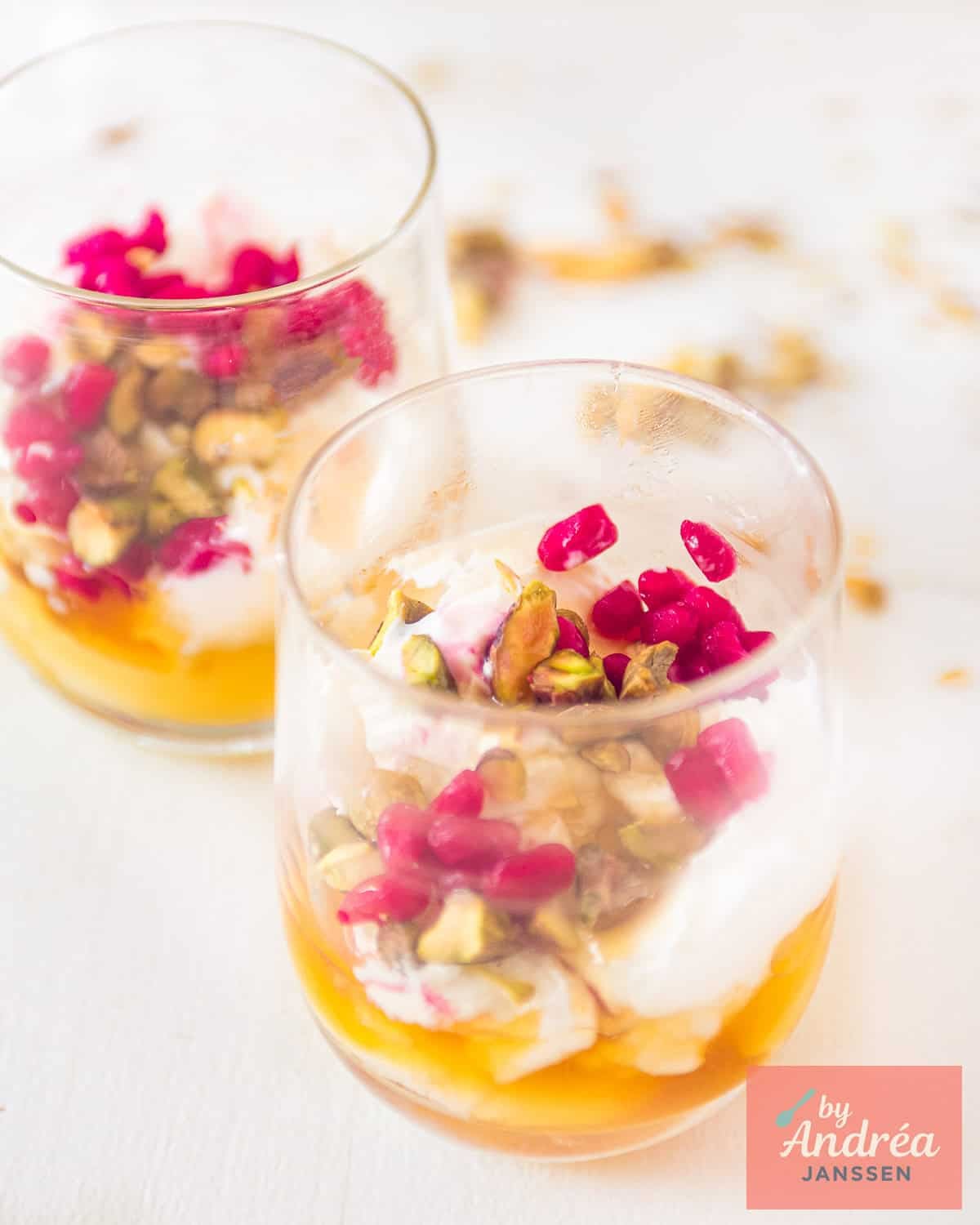 Two dessert glasses filled with homemade strained yogurt with honey and pistachio, placed diagonally behind each other on a white background.