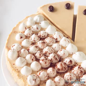 A square photo with part of an Irish Coffee tart cheesecake on a white surface. A point has been cut out at the top.