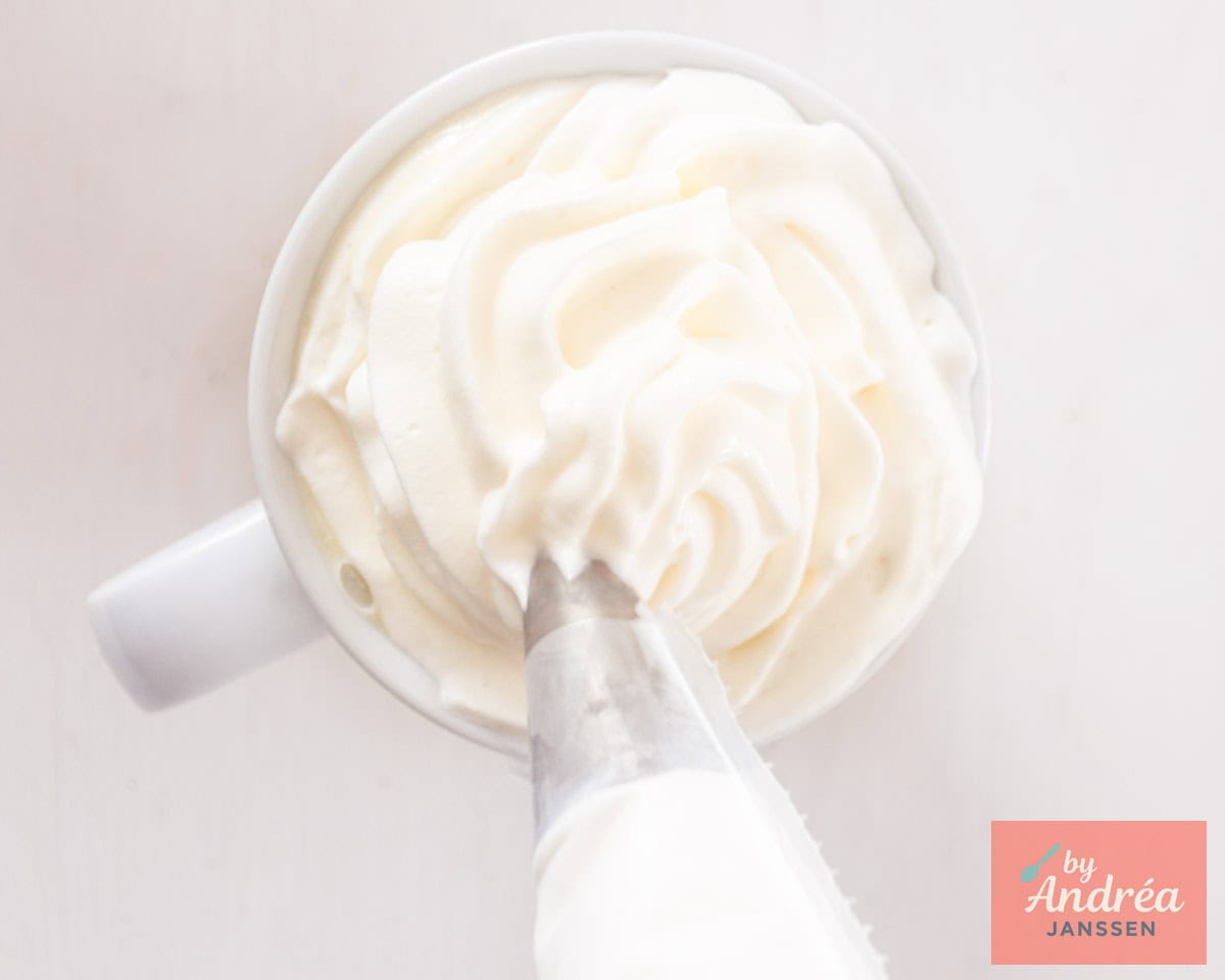 Whipped cream is piped on top of white hot chocolate