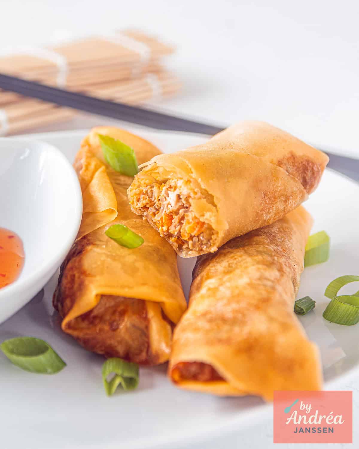 Three spring rolls, deep fried, one open so you can see the filling on a white plate.