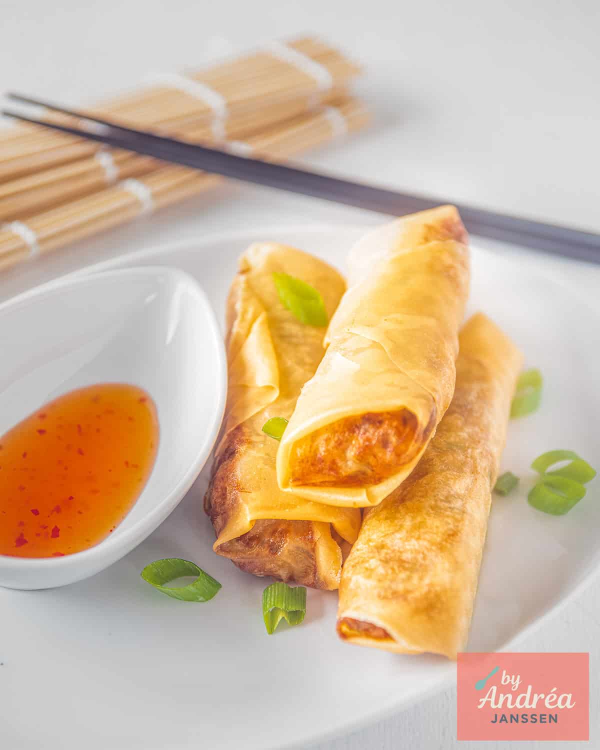 A white plate with three Vietnamese style fried spring rolls and some chili sauce aside.