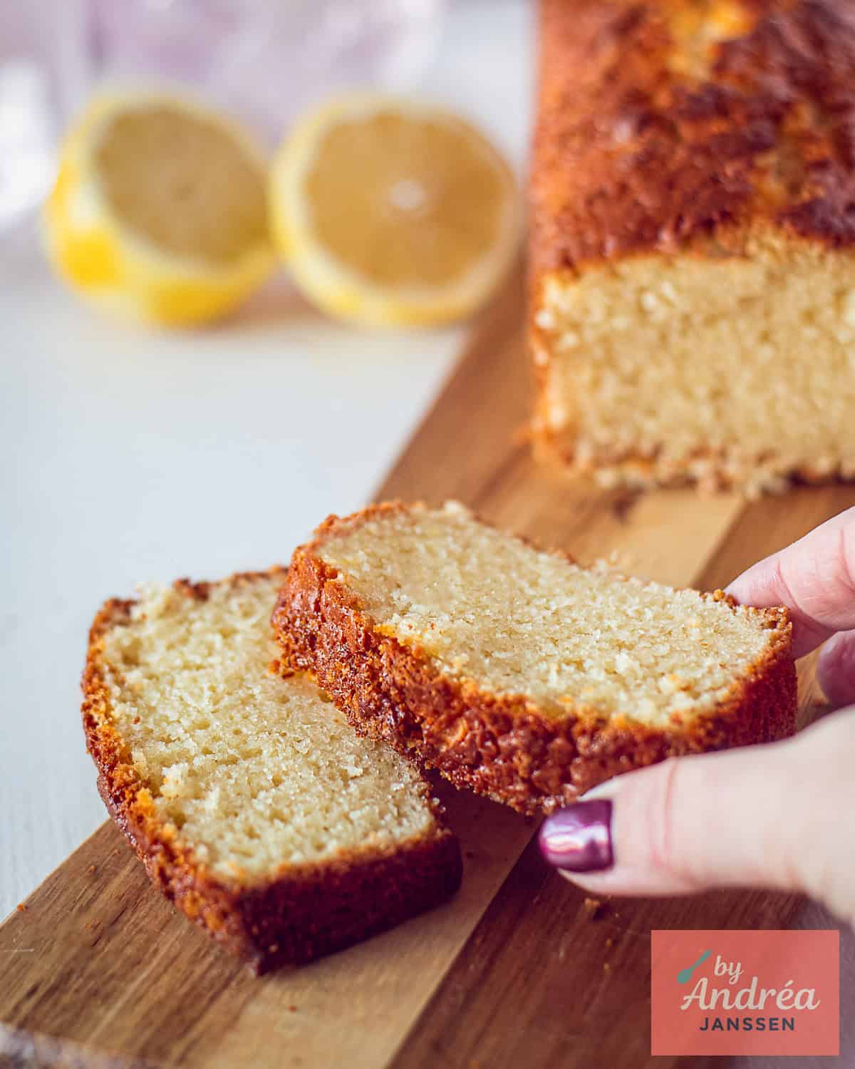 A wooden board with two slices of lemon olive oil cake (more of the cake in the back)