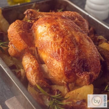 A square picture of a roasting pan filled with roasted chicken and potatoes, bacon and rosemary