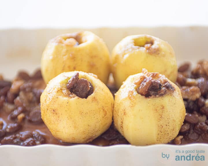 Stuffed apples on a bed of raisins and water in a white baking dish