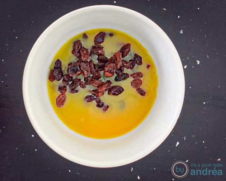 A white bowl with orange juice in which raisins are soaked.