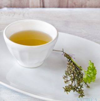 Homemade vegetable stock in a bowl with some herbs