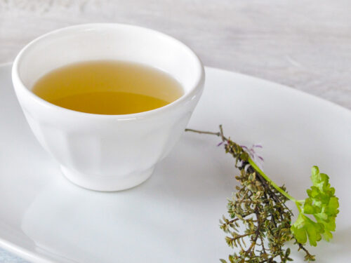 Homemade vegetable stock in a bowl with some herbs