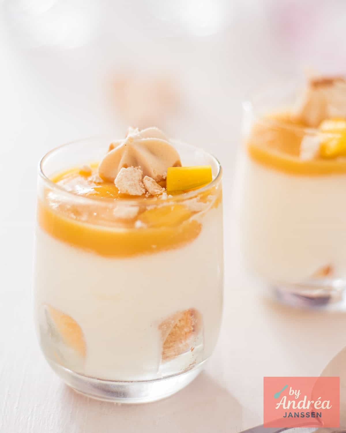 Een foto met twee glaasjes schuin achter elkaar gevuld met Mango Toetje met Witte Chocolade en Gin