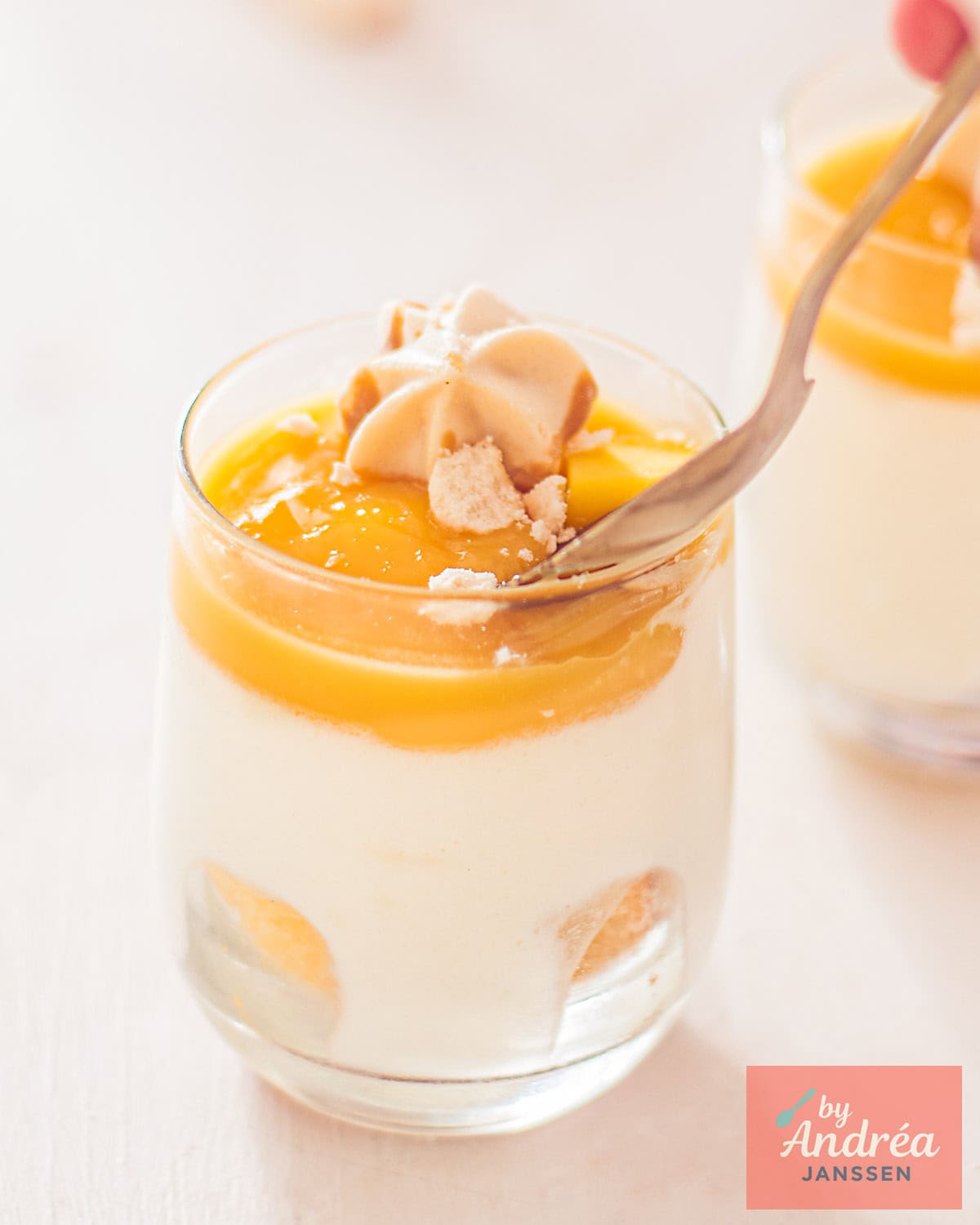 Een glas gevuld met mango gin en witte chocolade mousse. Een lepel schept een hapje eruit.