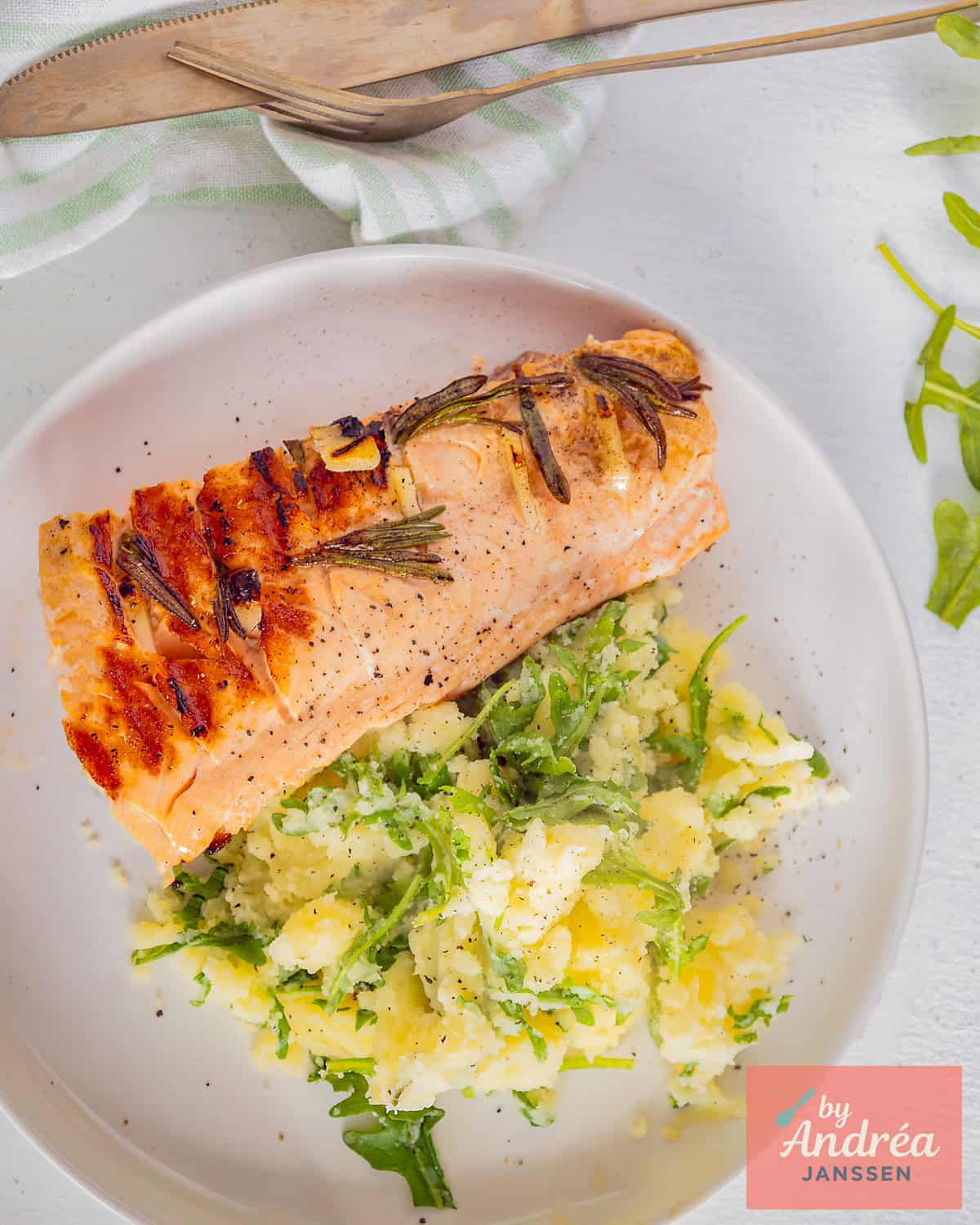 Een foto van bovenaf van een stamppot van rucola en zalm, gegrild, met knoflook en rozemarijn.