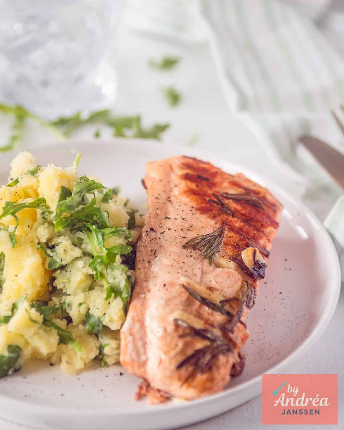 Een deel van een wit bord met een frisse rucolatsamppot met gegrilde zalm.