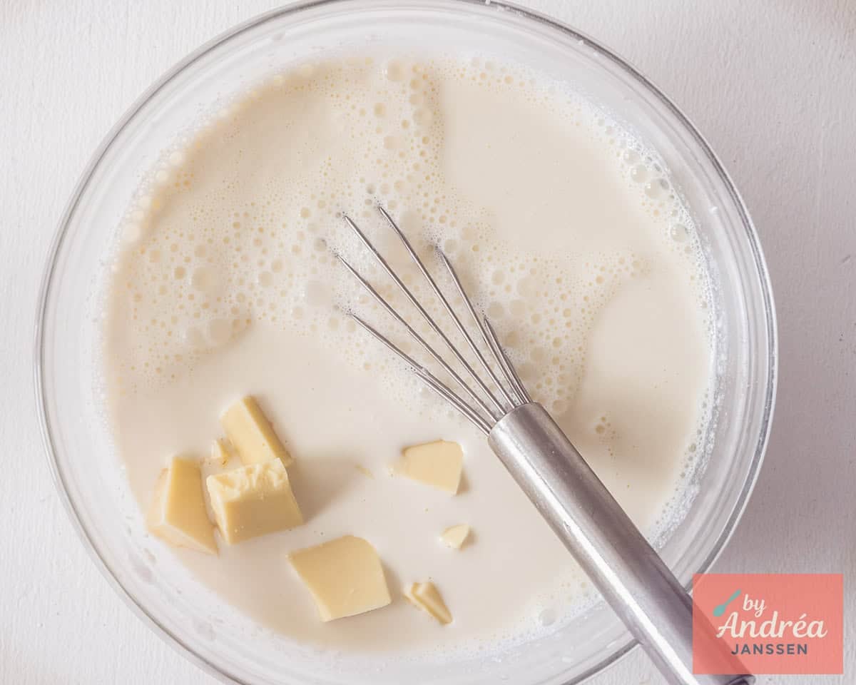 White chocolate added to hot cream in a glass bowl.