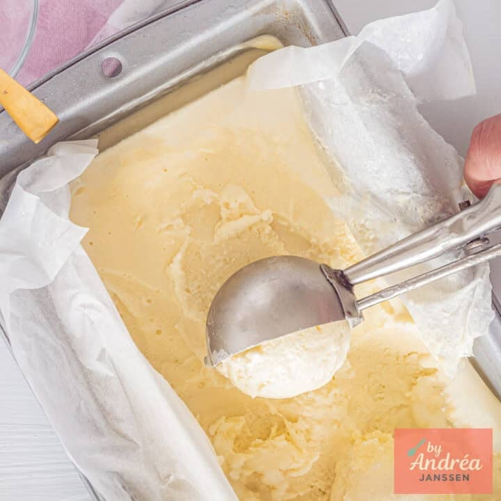 A square picture with a loaf tin with homemade chocolate ice cream. A scoop takes some ice cream out of it.