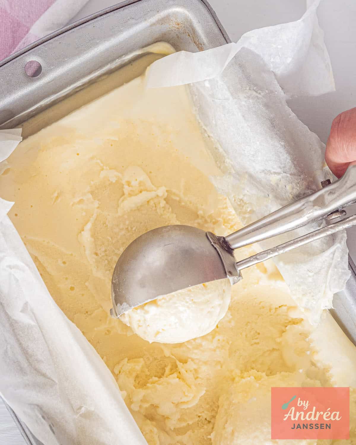 Top down picture of a tin filled with 4 ingredient white chocolate ice cream made from scratch. A scoop takes a ball.