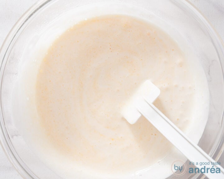 A glass bowl with sugar and eggs being mixed with a spatula.