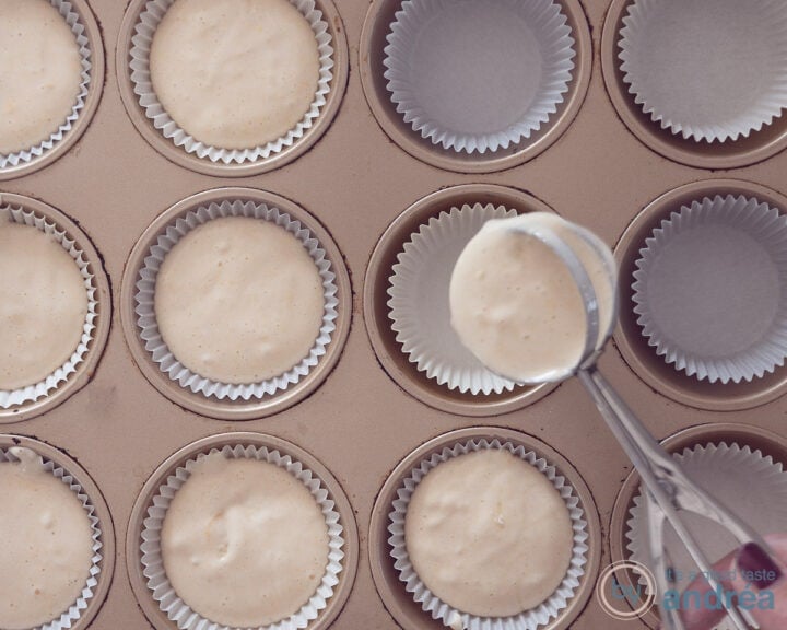 Paper cases in a cupcake shape into which batter is scooped with an ice cream scoop. Some molds are already filled.