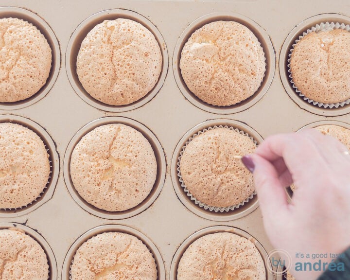 A cupcake mold with cupcakes in which holes are pierced with a skewer