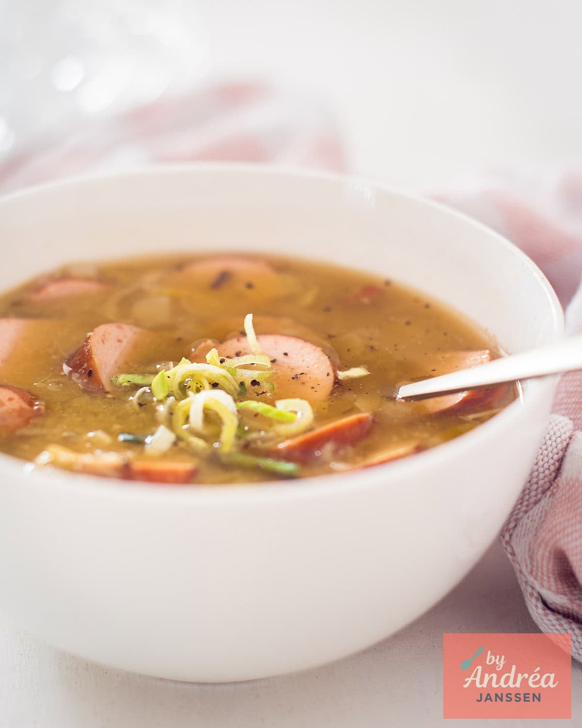 A portion of a white bowl of delicious pea soup with sausage and ham.