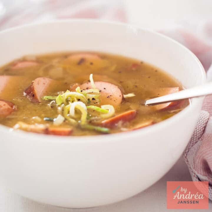 A square photo of a white bowl of pea soup with sausage and ham, just like grandma makes.