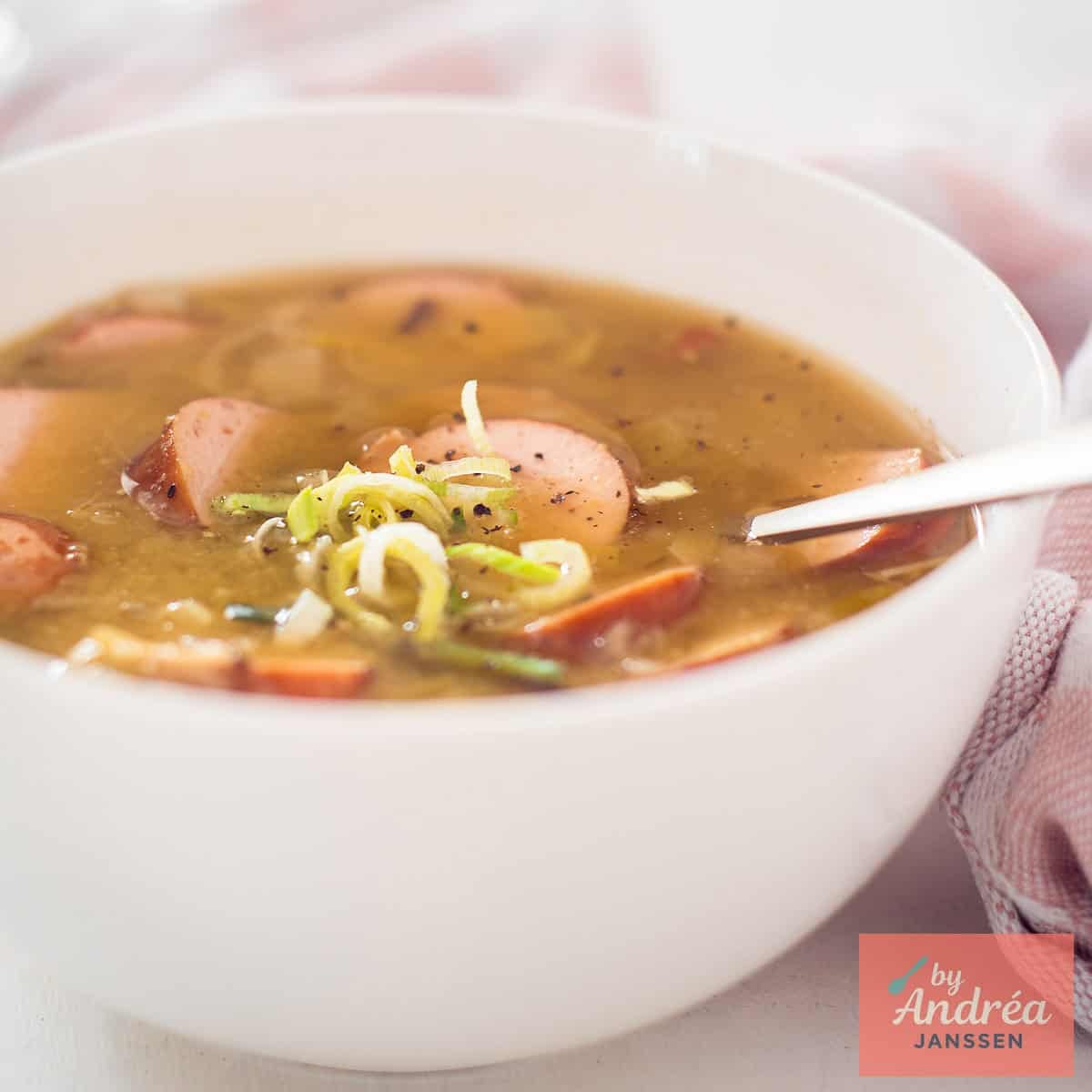 A square photo of a white bowl of pea soup with sausage and ham, just like grandma makes.