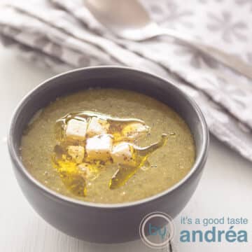 A square photo with a gray bowl of spinach soup made from fresh spinach, feta and olive oil. A gray white tea towel in the background.
