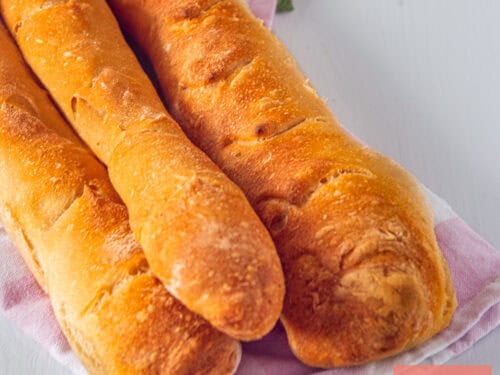 A square photo with three homemade baguettes in a stack on a tea towel.