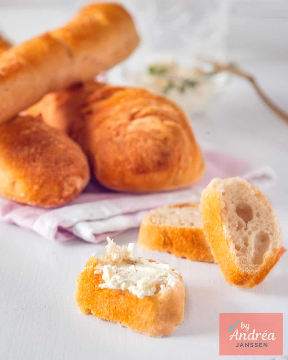 Three baguettes in the background. In the foreground, three slices cut, 1 spread with herb butter.