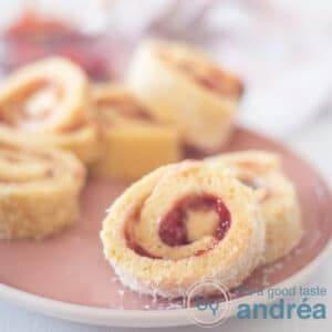 Square photo with a pink plate with cake rolls filled with jam and buttercream
