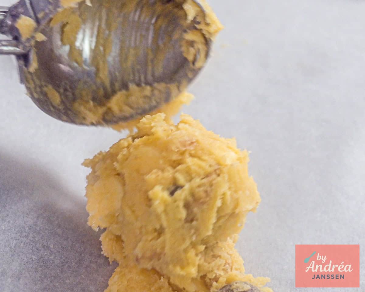 Cookie dough is placed on baking paper with an ice cream scoop.