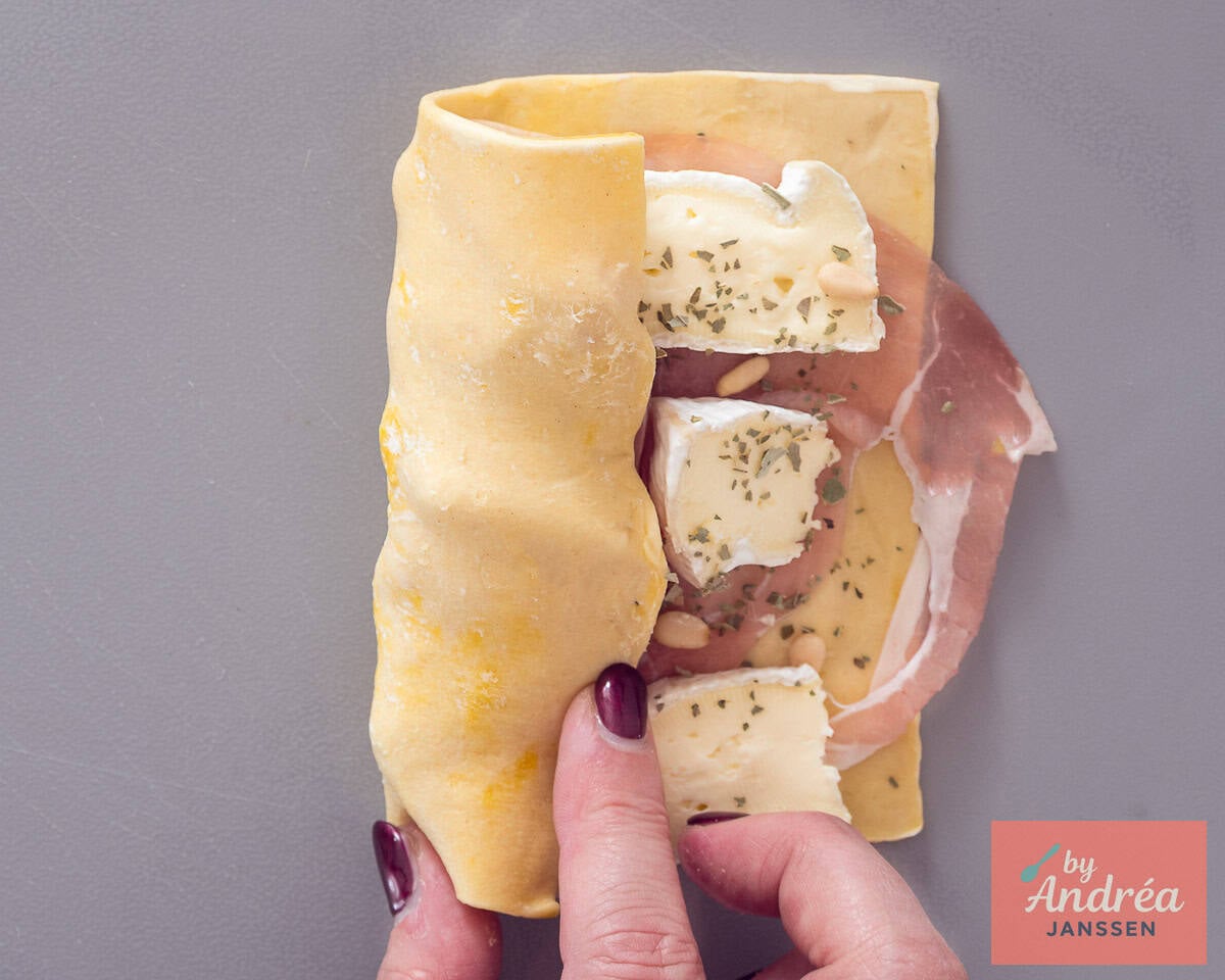 Rolling up puff pastry filled with camembert, bacon, and basil