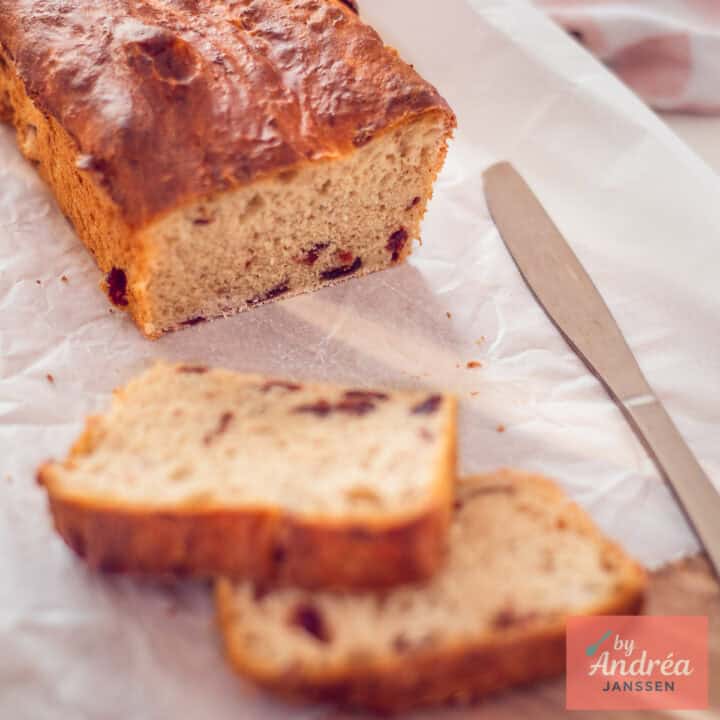 A square picture with a cranberry loaf on a baking paper. Two slices cut off.