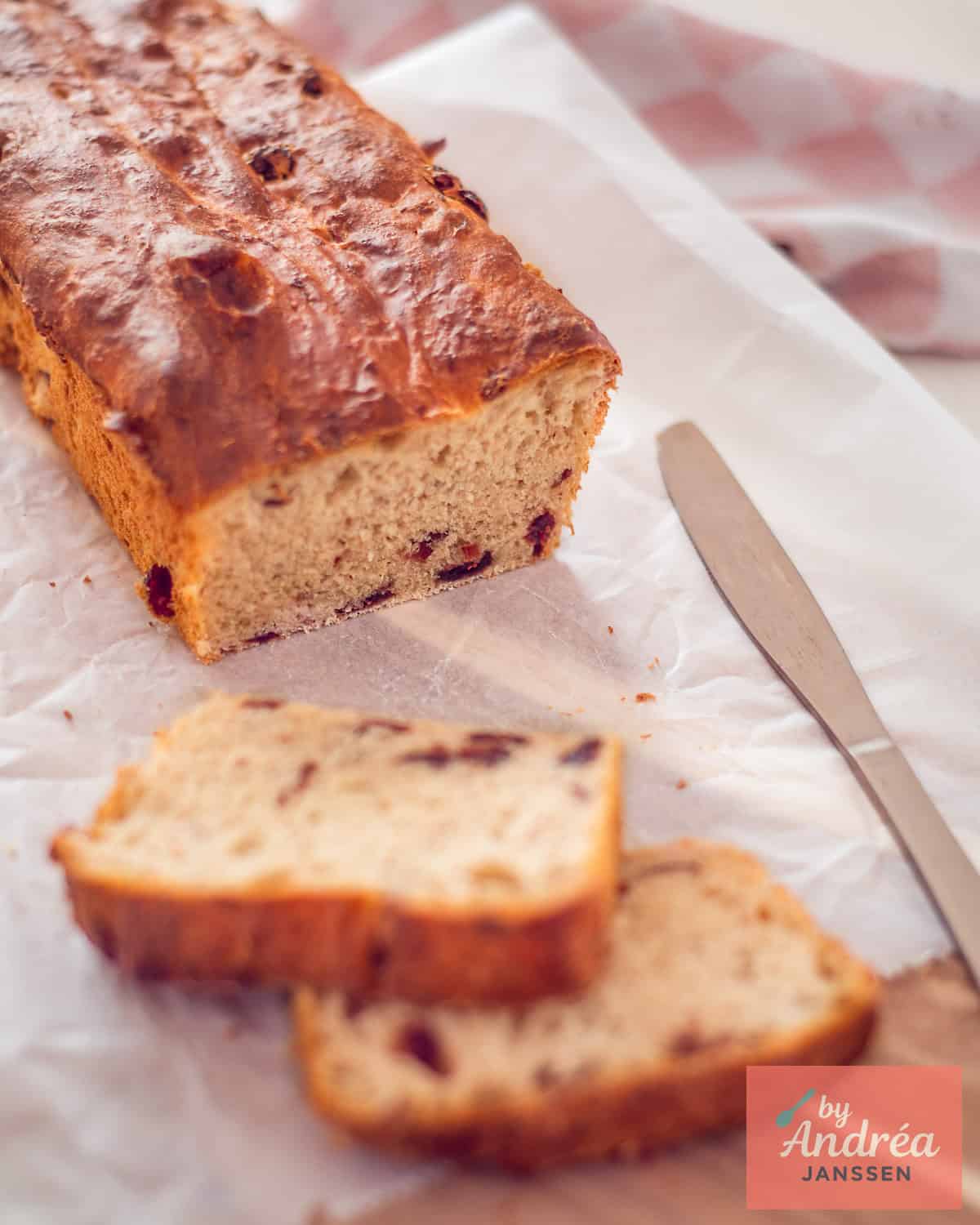Cranberry bread on a white backing paper with two slices in front.