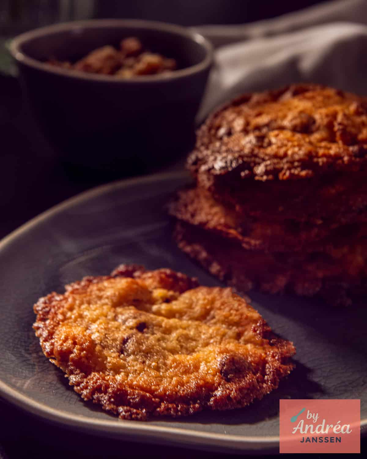 A bowl of double chocolate cookies with walnuts. A cookie in the foreground, a small stack in the background.
