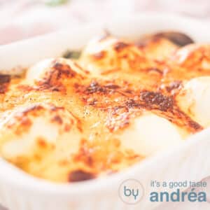 A square photo showing a white baking dish filled with egg au gratin on a bed of spinach.