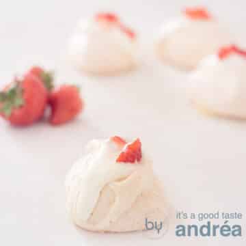 A square photo with rose meringue in the foreground and three in the background. Left strawberries.