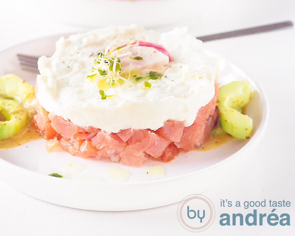 A wide shot with a tower of smoked salmon, goat cheese mousse on a bed of cucumber against a white background.