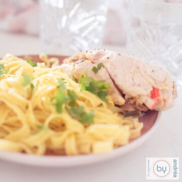 A square photo with a pink plate with tagliatelle and stuffed chicken with dates and surimi