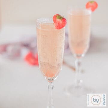 A square photo of two champagne flutes filled with strawberry prosecco cocktail with a strawberry garnish.