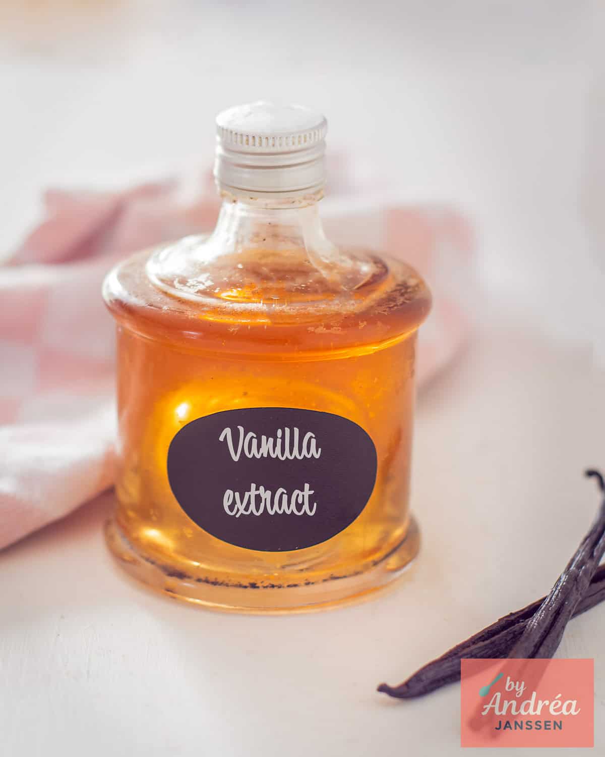 A bottle of vanilla extract on a white background with some vanilla pods in front.